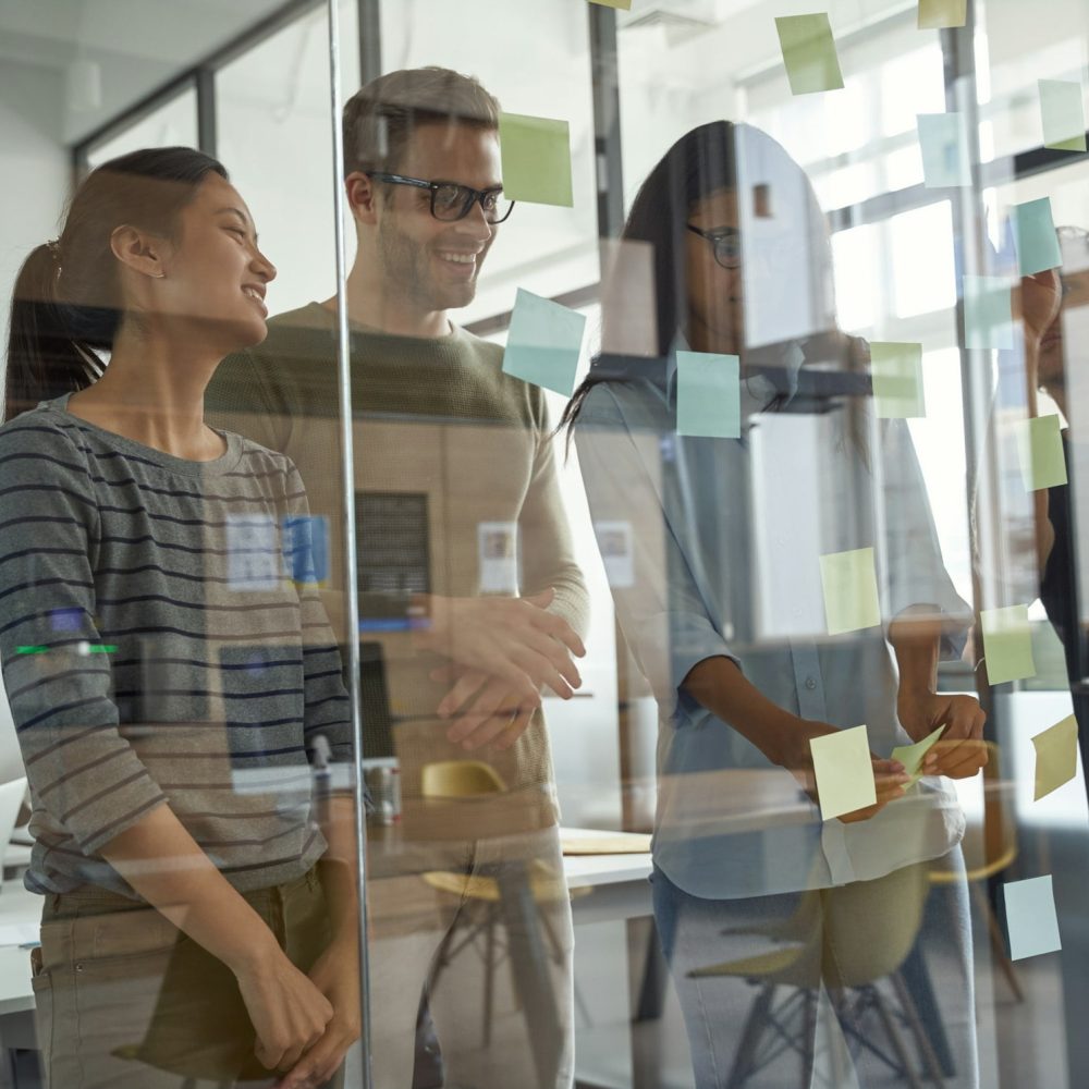 Brainstorming concept. Group of happy creative business people looking at sticky notes on glass